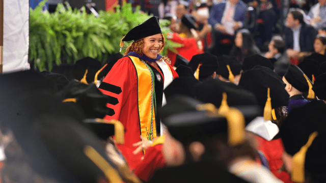 A graduate smiles as she walks down the aisle at commencement.