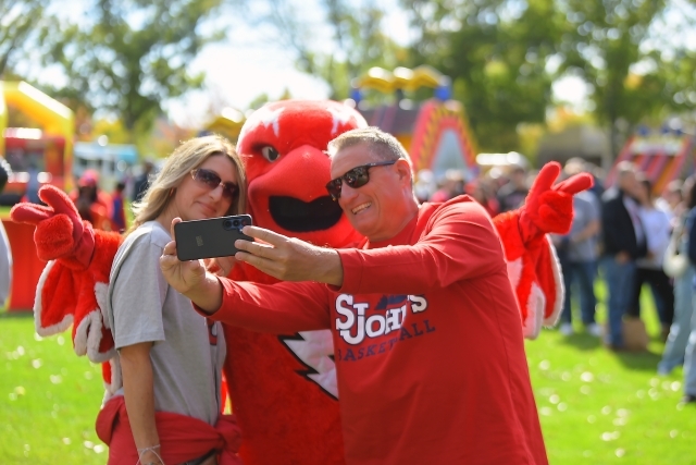 Two people taking a selfie with Johnny Thunderbird, the school mascot.
