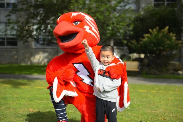 A young child taking a photo with Johnny Thunderbird, the school mascot.