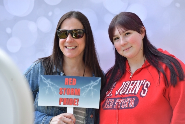Two people in a photo booth taking a photo with a sign.
