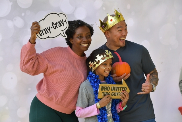Two adults and one child in a photo booth using crown and sign props