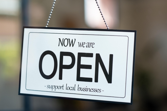 A sign that reads, "Now we are OPEN support local business" in the window of a door
