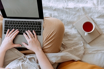 Stock Image of a person using a laptop and cup of tea on a white blanket