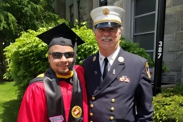 Sgt. Gabriel Vazquez ’18CPS in his cap and gown at commencement with Eugene Carty '73GEd in his FDNY uniform