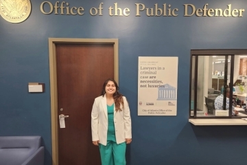 Nicole Castillo Guiracocha stands in her office's waiting room under a sign reading Office of the Public Defender.