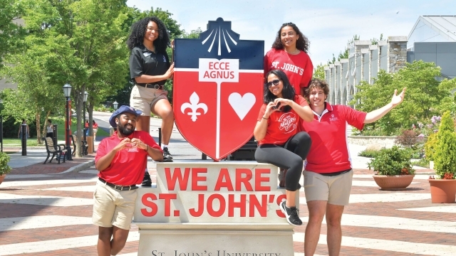 Students posing on a statue of the St. John's University logo