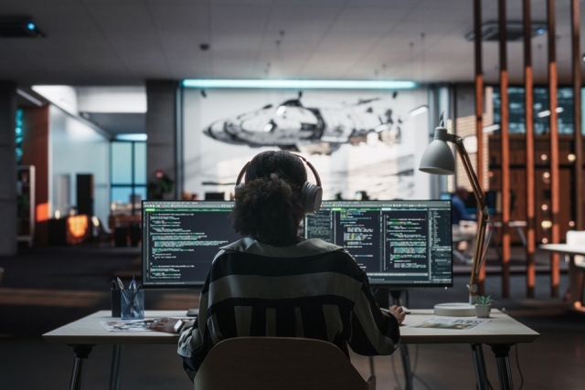 Girl sitting at computer desk with technology displays all around