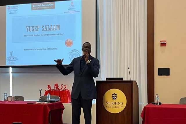 Yusef Salaam presenting next to podium and in front of projector screen