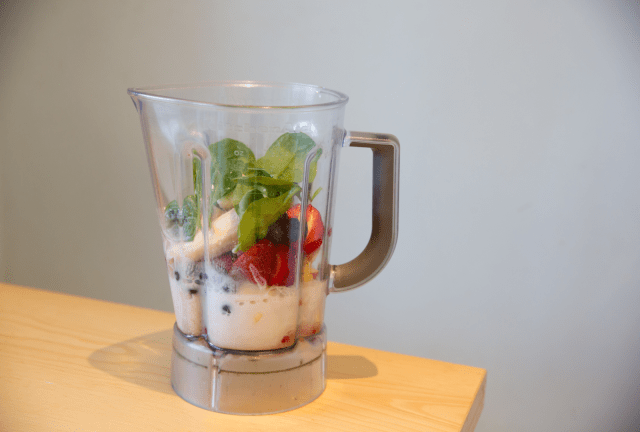 Smoothie blender with fresh fruits, leafy greens, and other healthy ingredients ready to be blended into a nutritious drink.