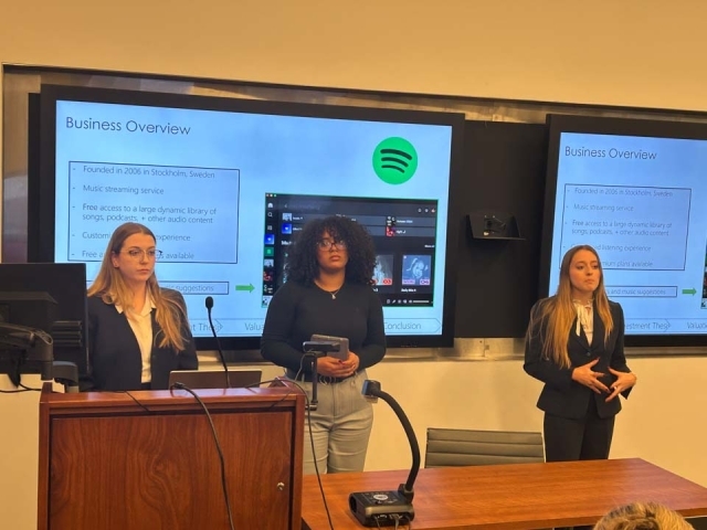 Three female Tobin students presenting in front of projector screen