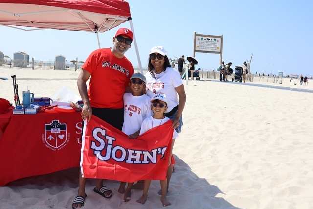 St. John's Alumni and family holding a SJU flag while cleaning up Jones Beach