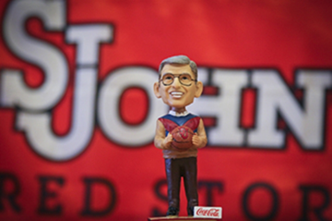 Bobblehead of Lou Carnesecca infront of St. John's flag