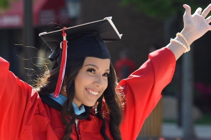 Female student in cap and gown raising arms in excitement