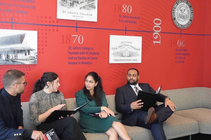 Four St. John's University students sitting on a couch in business attire talking to each other.