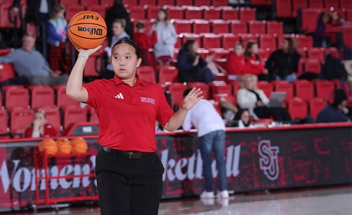 Women holding a basketball in a red shirt behind stadium seating