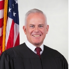 St. John's University Alumni Judge Horan in robe standing infront of American flag